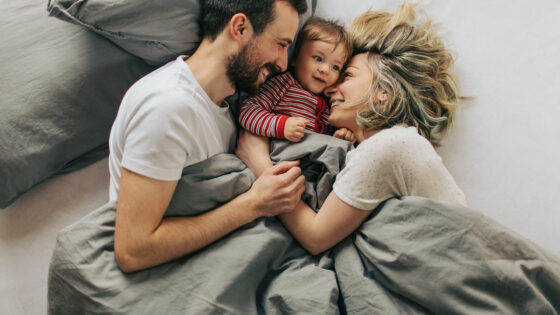 parents cuddling toddler in bed