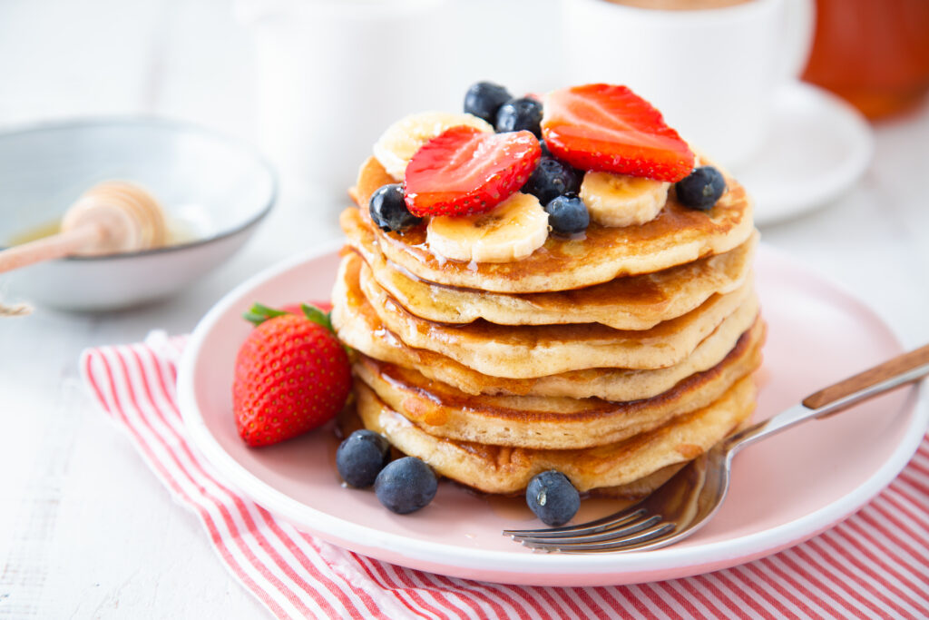 Fortisip Banana Recipe: stack of homemade pancakes with strawberries, banana and blackberries