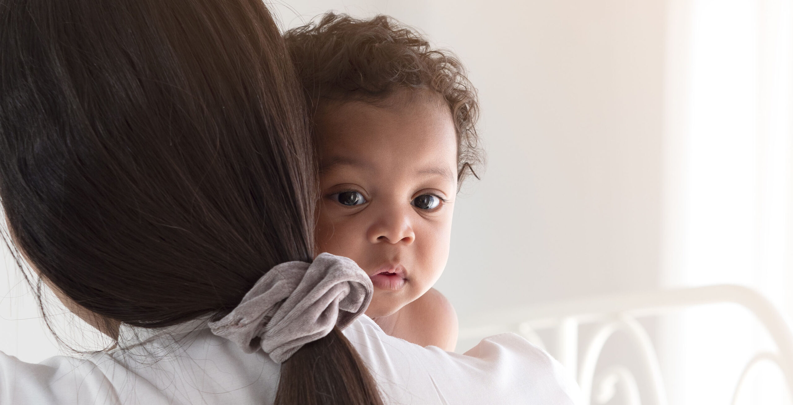 Mother facing away, baby in her arms looking over her shoulder.