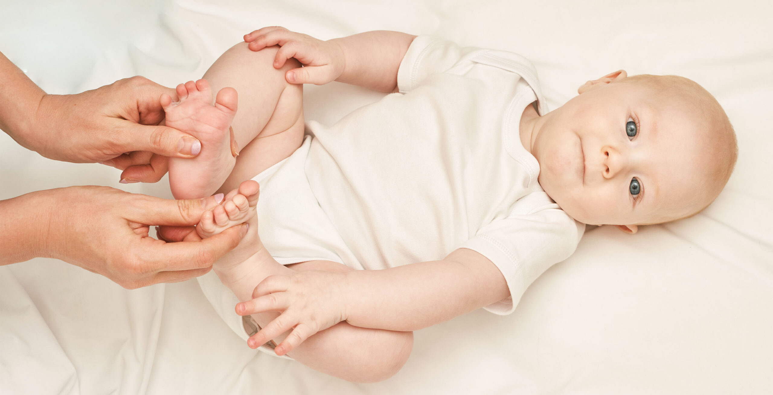 Baby lying on their back with soles of feet together as mum’s hands hold their toes.